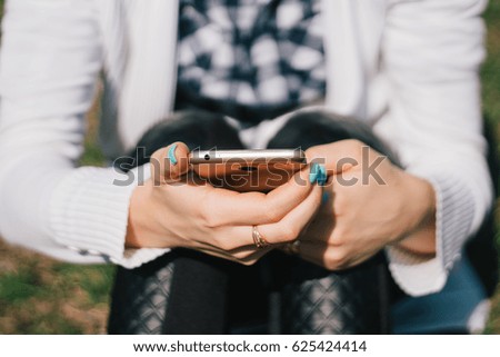 Beautiful young European girl sits on the grass in the park and uses a smartphone, concepts of using gadgets in a natural environment 