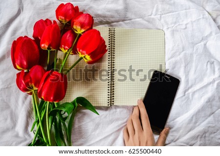 Clean notebook, phone and bouquet of red tulips