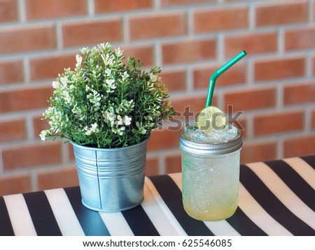 A tasty iced honey lemon soda decorated with sliced lime place with flower tin can on a black and white stripe table, brick background