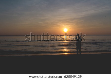 Silhouette. A man is taking a picture in the sunrise at seaside.