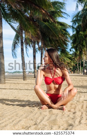 Relaxed girl enjoying tropical beach. Young beautiful Brunette woman in red bikini practicing morning or evening meditation in nature at the beach