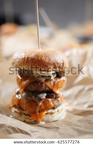 Delicious big fat double hamburger.American fast food restaurant menu dish.Grilled huge burger with sauce,pork & burner cheese served on brown paper in cafe.Fast food close up