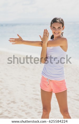portrait of sporty woman smiling while doing arms stretching at the beach