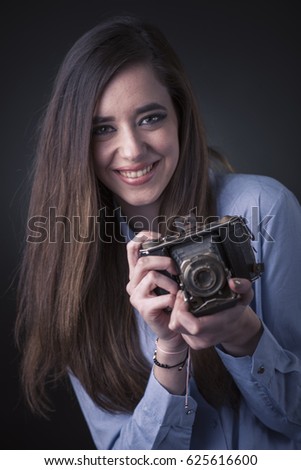 Smiling young woman in a blue shirt holding an old, vintage camera