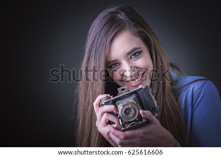 Smiling young woman in a blue shirt holding an old, vintage camera