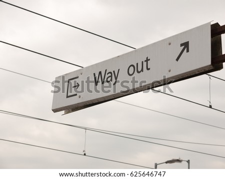 a sign with icons and arrows saying way out white and black with wires overhead train track directions way fare trains sky background