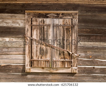 Closed wooden shutters secured by metal bar at rural log house