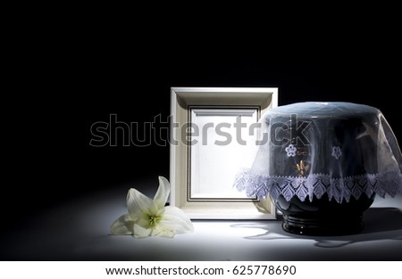 Black evangelical urn with blank mourning frame, and flower on dark background
