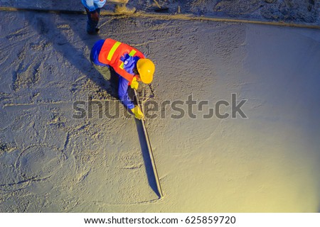 Mason worker leveling concrete with trowels, mason hands spreading poured concrete. Concreting workers are leveling poured liquid concrete on a steel reinforcement to form strong floor slab. Royalty-Free Stock Photo #625859720