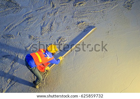 Mason worker leveling concrete with trowels, mason hands spreading poured concrete. Concreting workers are leveling poured liquid concrete on a steel reinforcement to form strong floor slab. Royalty-Free Stock Photo #625859732