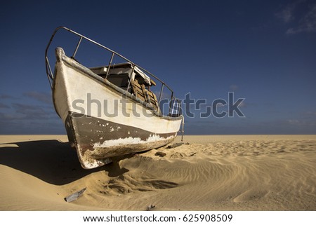 An old, abandoned fisher's boat on a deserted beach. The stark blue sky is in contrast with the dull sand which is washed out from under the boat. The warm filter adds to the atmosphere of the picture