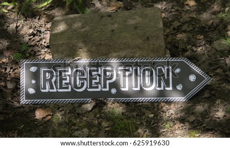 Reception this way sign, black sign with white text with stone and garden background
