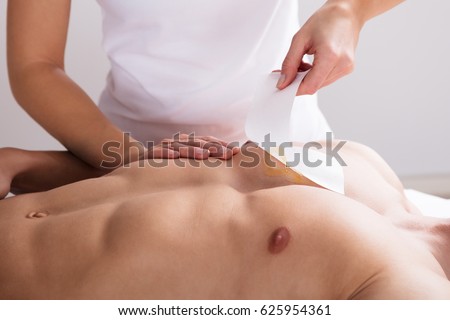 Close-up Of A Woman Waxing Man's Chest With Wax Strip Royalty-Free Stock Photo #625954361