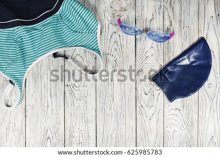 Swim items (swimsuit, swimming goggles, swimming cap) on the wooden background. Top view