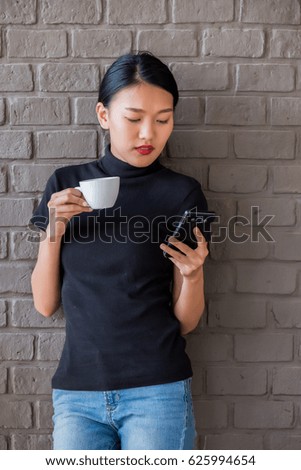 Young Asian woman using smartphone for browsing internet, personal chat, and social media while sipping coffee in coffee shop. Weekend lifestyle concept with vintage filter effect