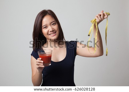 Young Asian woman with tomato juice and measuring tape on gray background