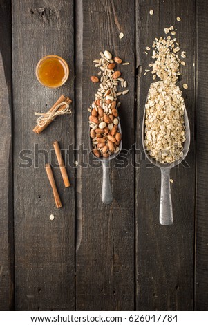 Natural products in iron vintage scoops on wooden granary boards. Hercules flakes (oat flakes), sunflower seeds, fresh peanuts, hazelnuts, honey. Ingredients for granola or oatmeal. Useful breakfast.