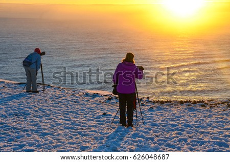 Two female photographers with tripod waiting to the sunset over the sea.