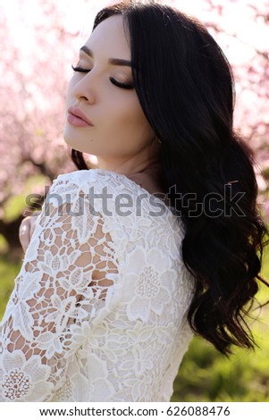 fashion outdoor photo of gorgeous young woman with dark hair  in elegant dress posing in garden with blossom peach trees