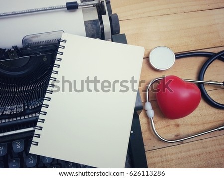 notebook, red heart, stethoscope and typewriter on wood table, business and healthcare concept, process vintage tone
