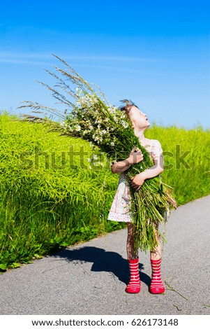 summer portrait of cute little girl with chamomile bunch. child gathering daisies on rural field. picking flowers for midsummer celebration.
