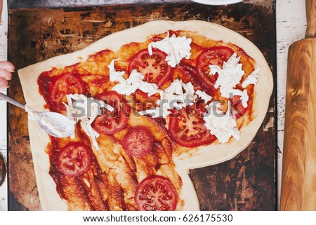 Love pizza. Baked heart-shaped homemade pizza on a cutting board on white wooden background. Close up
