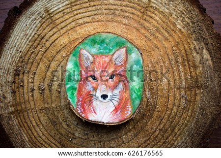 Painted forest animal on a cut piece of wood. Beautiful natural paint colors. Background of brown wooden cut tree trunk. Red fox