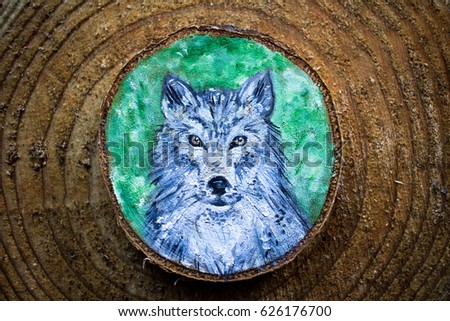 Painted forest animal on a cut piece of wood. Beautiful natural paint colors. Background of brown wooden cut tree trunk. Grey wolf