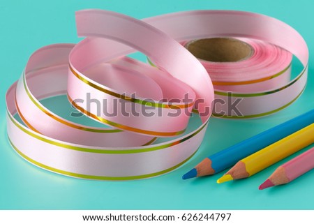 Pink ribbon tape and pen on aquamarine background. Art concept