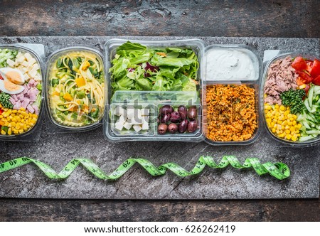 Various Healthy lunch boxes in  plastic package and green measuring tape on rustic background, top view. Dieting food concept. Royalty-Free Stock Photo #626262419