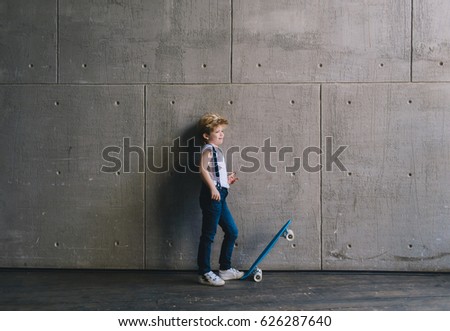 Little boy standing with a skateboard at a wall