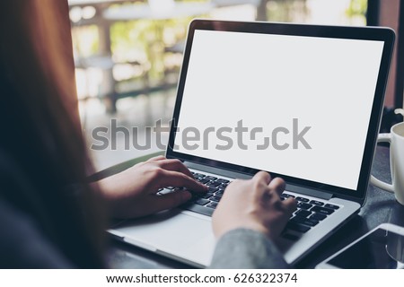 Mockup image of business woman using and typing on laptop with blank white screen and coffee cup on glass table in modern loft cafe Royalty-Free Stock Photo #626322374