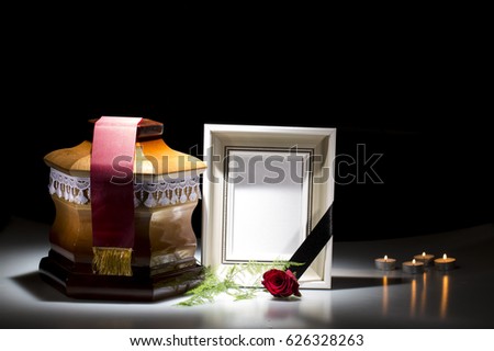 Wooden cemetery urn with blank mourning frame and red rose, candle lights on dark background
