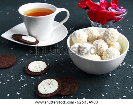 Red terry tulips on notes and round sweets with almonds and coconut in a glass bowl on flower petals on a dark horizontal background.The concept of the feast