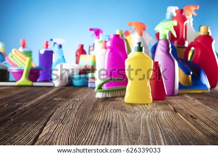 Spring cleanup theme. Variety of colorful house cleaning products on a rustic wooden table and blue background. 