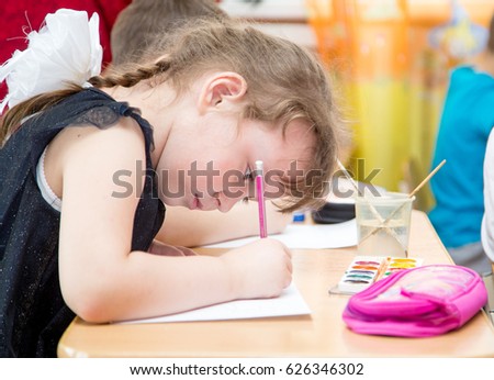 girl draws paints with a pencil, head low, bowed over the picture