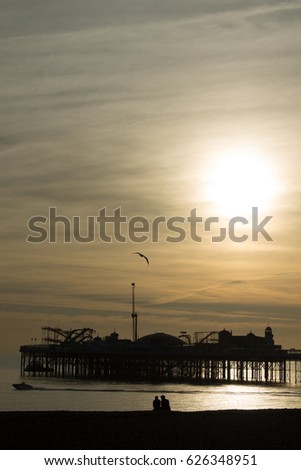 A couple on the beach at Subset silhouetted against Brighton Pier