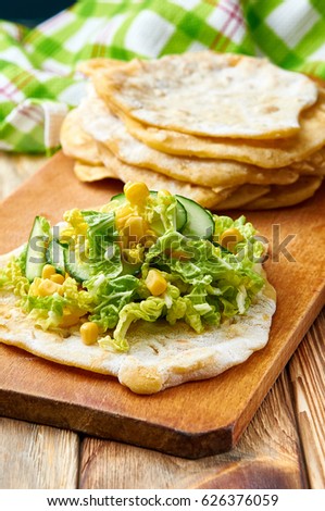 Simple rustic corn tortillas with fresh vegetable salad. Beautiful picture of food in green spring tones. Salad from corn, cucumbers and Peking cabbage. Food on a wooden board. 