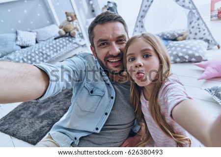                                Funny selfie with dad. Self portrait of young father and his little daughter taking selfie while sitting on the floor in bedroom