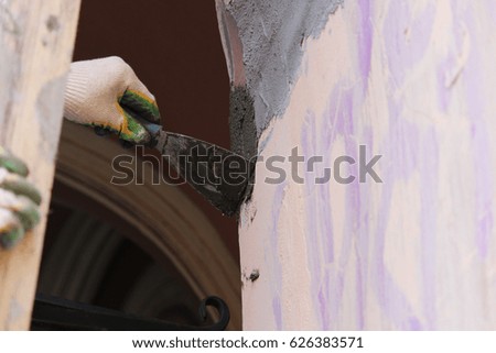Construction worker wearing worker overall with wall plastering tools renovating apartment house. Plasterer renovating outdoor walls of old house. Construction finishing works.