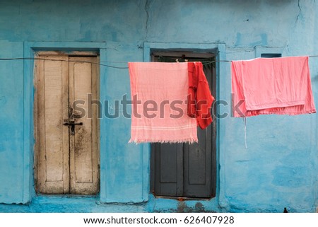 Pink clothes hanging in front of bright blue texture background with doors in Bangalore, India Royalty-Free Stock Photo #626407928