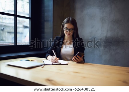 Confident female administrative manager of company noting contacts of banking service browsing information via modern smartphone connected to wifi,formally dressed journalist dialing number on mobile
