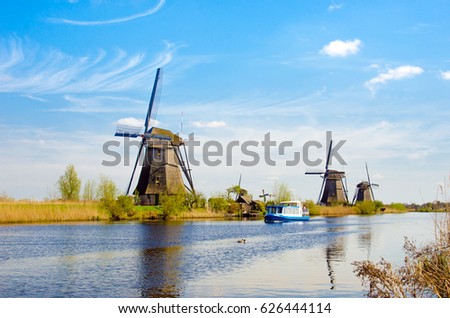 Fascinating scenic picture of windmills and boat on river in Kinderdijk, Netherlands, Europe against the backdrop of a cloudy sky.