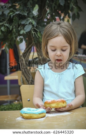 A small charming child came to the food court in the mall and was about to eat a donut. A child is a girl 4-5 years old.