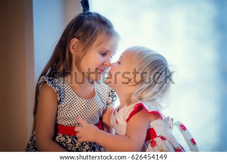 Sisters in dresses kissing at the window of the house