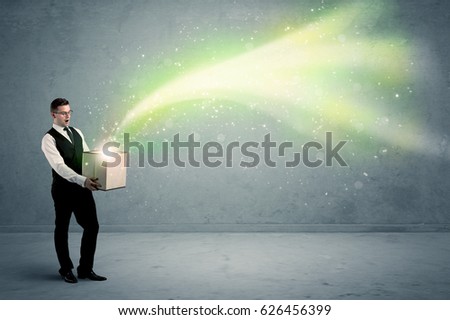 Bright yellow, green light beams escaping a cardboard box held by young elegant male business person in stylish suit concept.