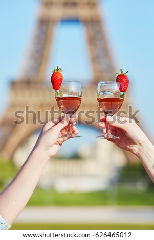 Women hands holding two glasses of rose wine with the Eiffel tower in the background. Summer picnic in Paris, France