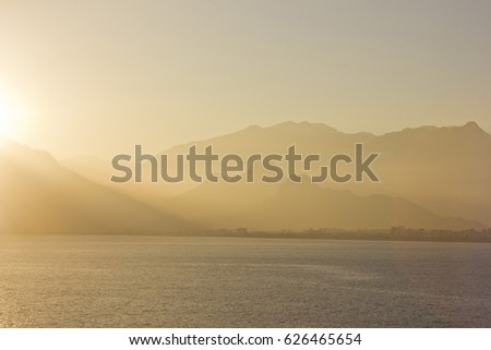yellow sunset above sea with mountains on background