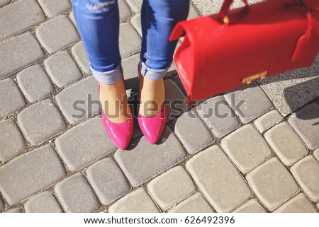 Woman's legs in blue skinny jeans and pink leather classic high heels. Stylish elegant women with red handbag street look.