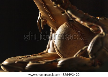 Close up image of an old used baseball and baseball glove on wooden table in black background